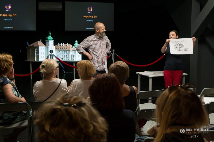 Spotkanie w sali multimedialnej, mężczyzna i kobieta prezentują rysunek na scenie