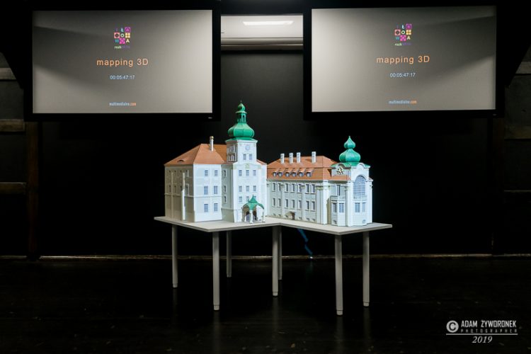 Makieta pałacu nastole, w tle dwa kolorowe monitory